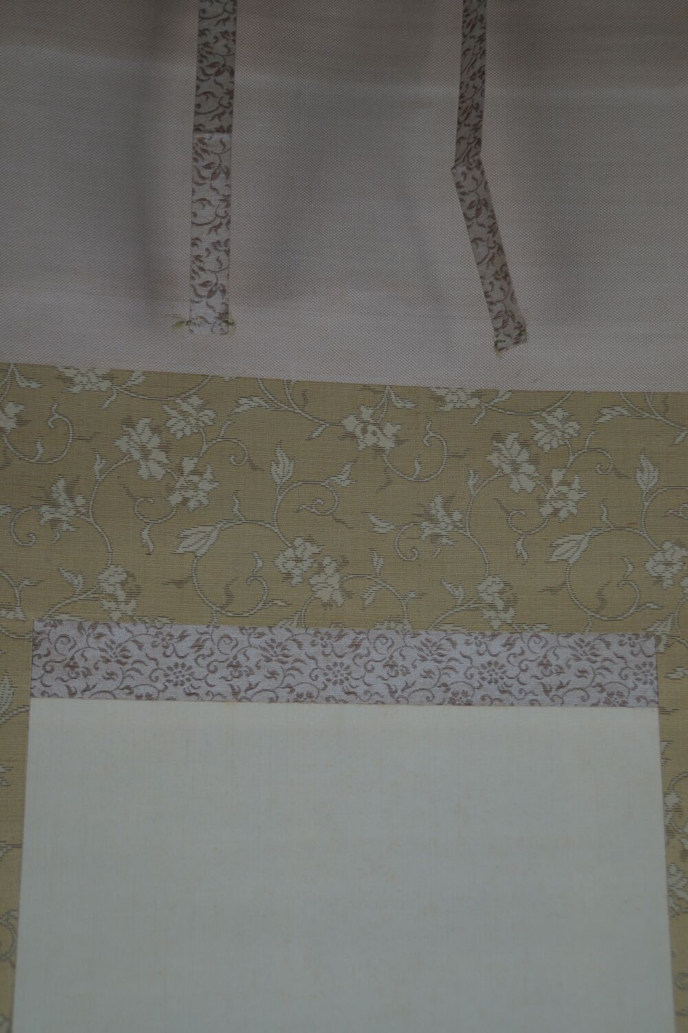 Detail view of the cream-colored silk mounting with floral brocade and hanging cords of the hanging scroll Rooster and Plum Blossoms