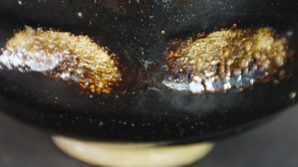 Extreme close-up of the two gold-colored glaze spots on the black glaze of the Chawan made of Raku ware
