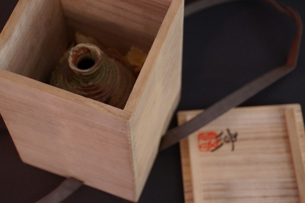 Bird's-eye view of the tokkuri lying in the opened storage box next to the lid with seal