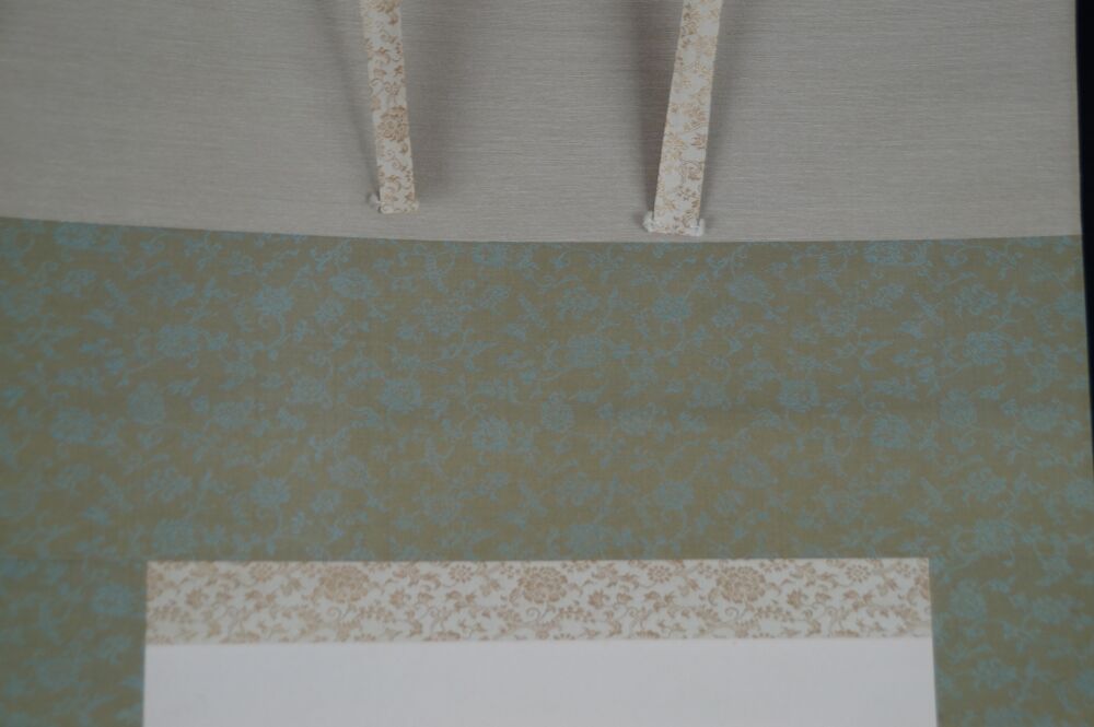 Detail view of the turquoise and gold silk mounting with hanging cords of the kakemono hibiscus blossoms and grasshopper