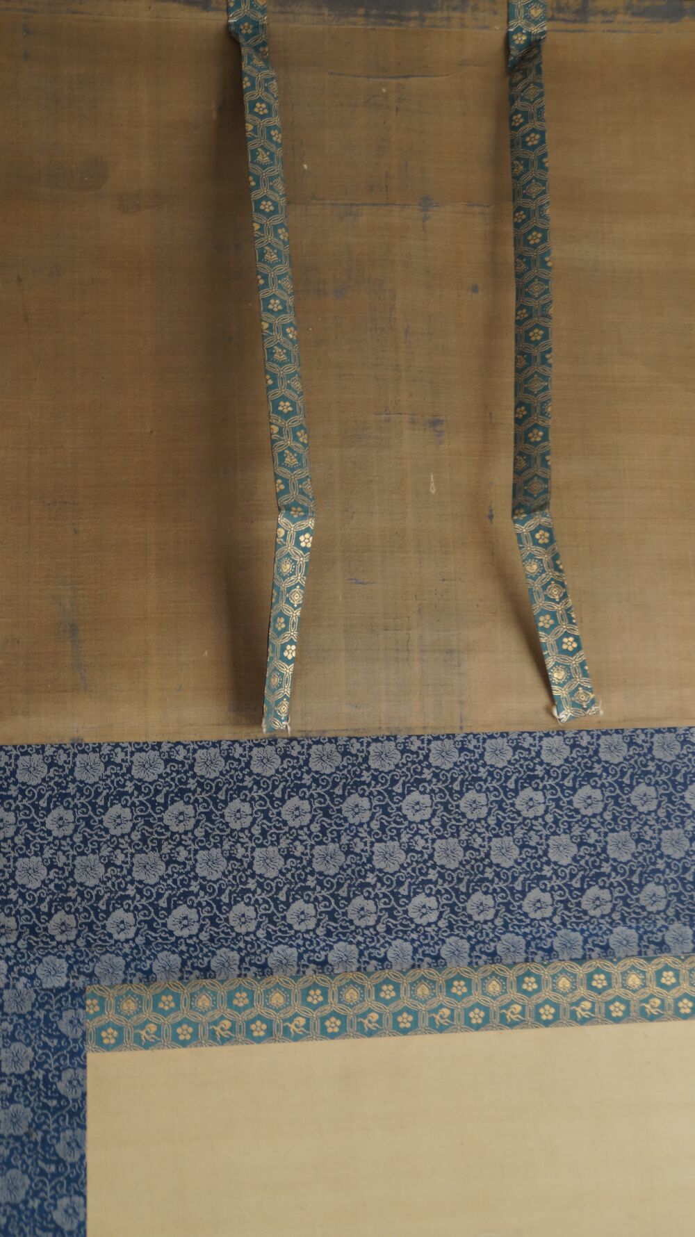 Detail view of the silk mounting with hanging cords and blue floral brocade of the hanging scroll Bodhidharma on the Path