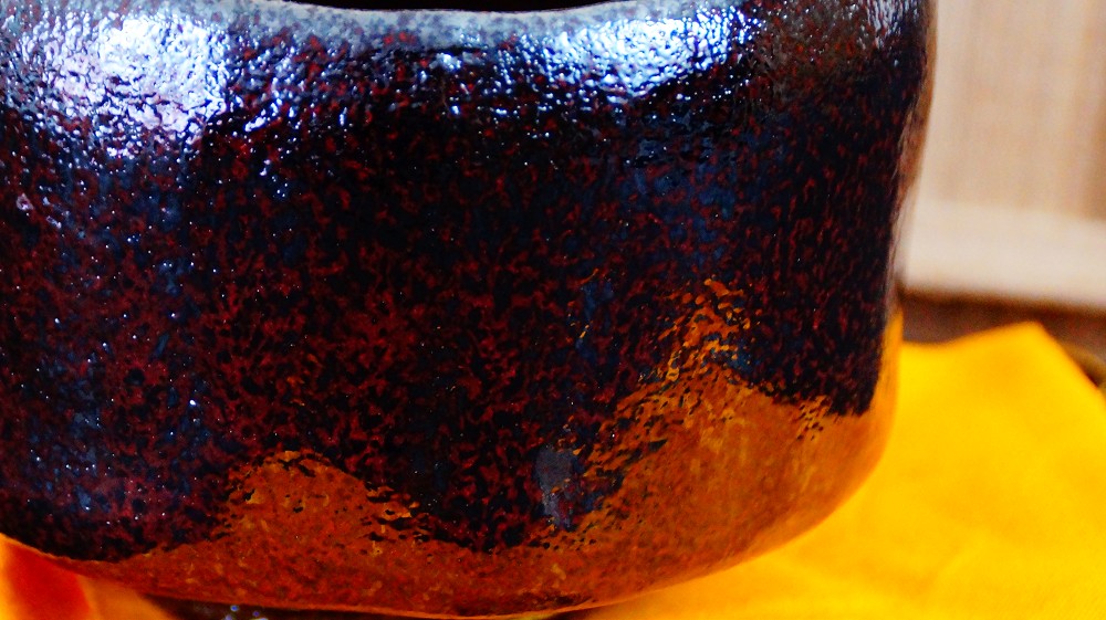 Close-up of the rough reddish-brown and black mottled glaze of the chawan made of Raku ware by Shoraku Sasaki