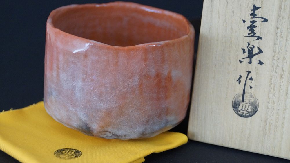 Further view of the chawan tea bowl on yellow cloth next to the storage box inscribed with Raku