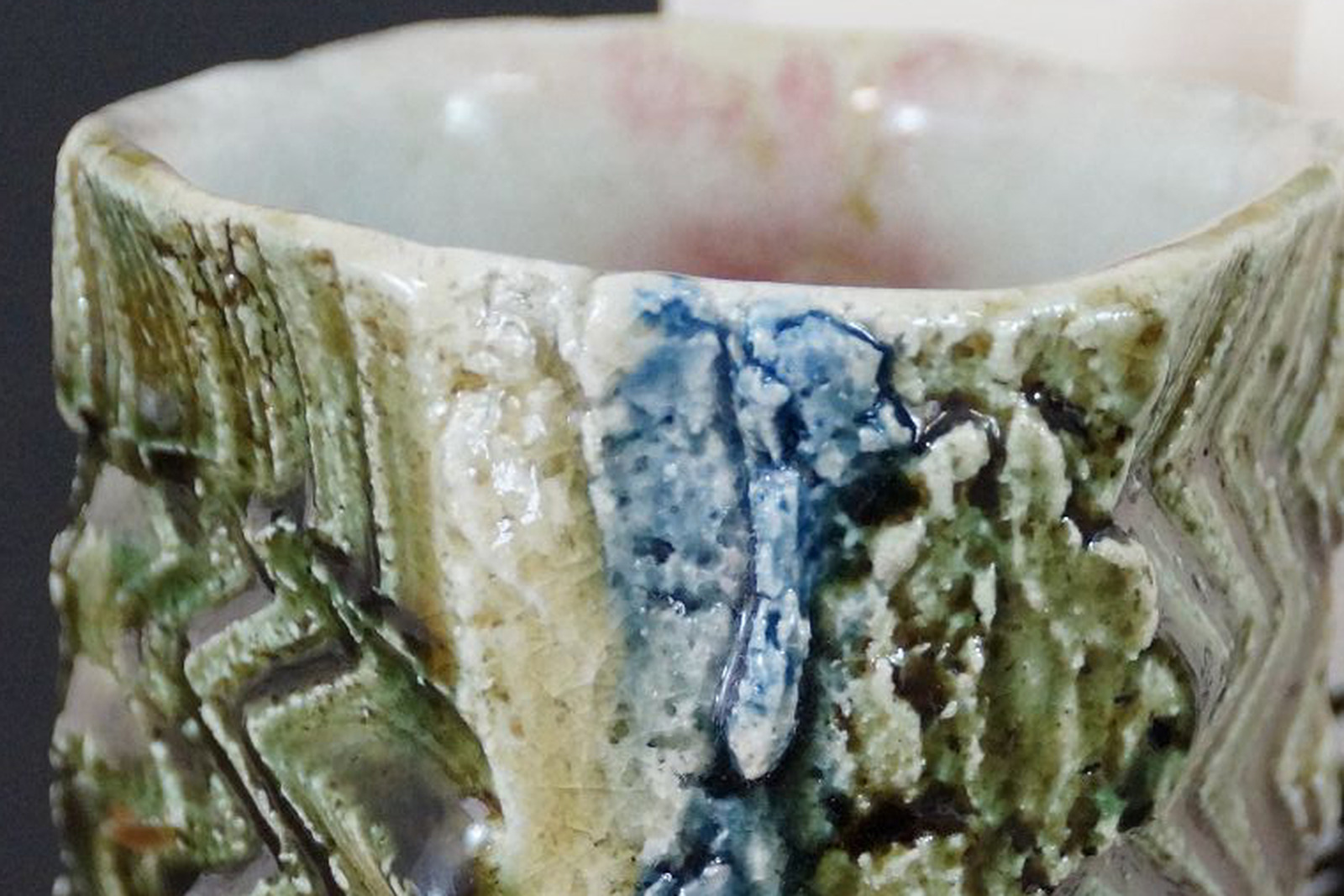 Rim and white interior glaze of a Japanese yunomi made of Oribe ware with green glaze and relief-patterned wall