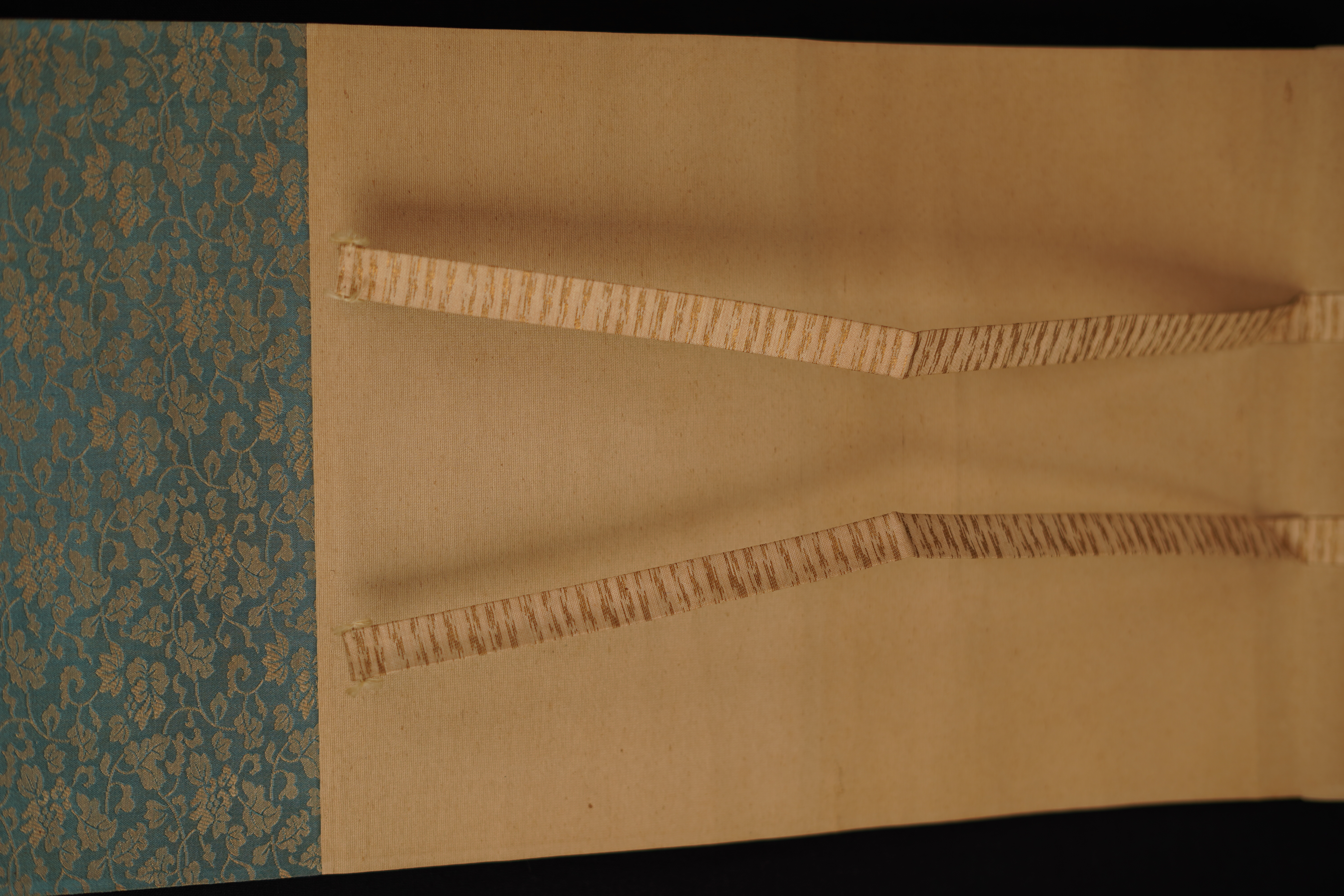 Detail view of the turquoise silk mounting with gold pattern and hanging cords of the hanging scroll Hanging Cherry Blossoms