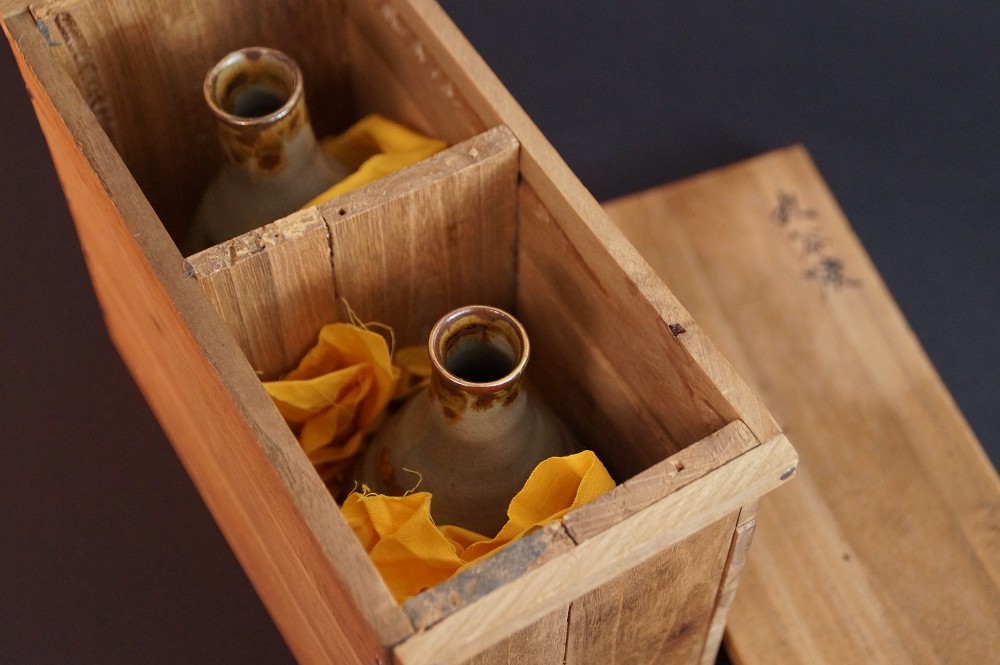 Die beiden Sake Flaschen eingebettet in orangefarbenes Tuch in den unterteilten Faechern der Aufbewahrungsbox
