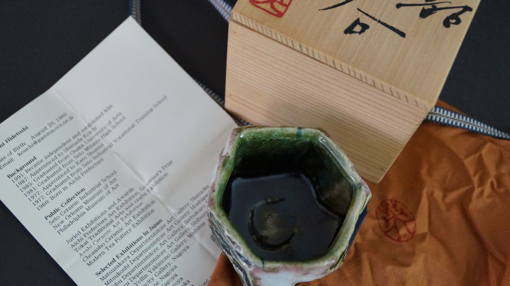 Guinomi sake cup next to storage box and the artist biography of Kawachi Hidetoshi