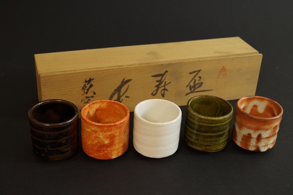 Five sake cups in a different order in front of the labeled wooden box set front view with storage box 2