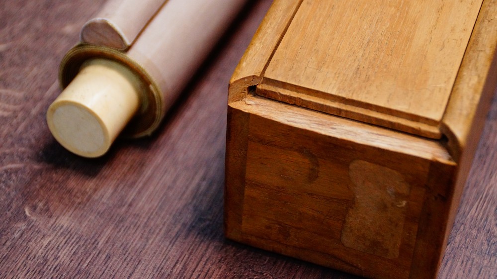 Hanging scroll with ivory scroll ends next to the opened wooden storage box