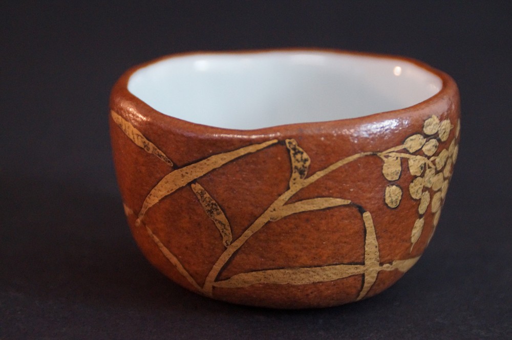 Side view of the sake cup with gold-colored branch and leaf motif on reddish-brown ceramic body