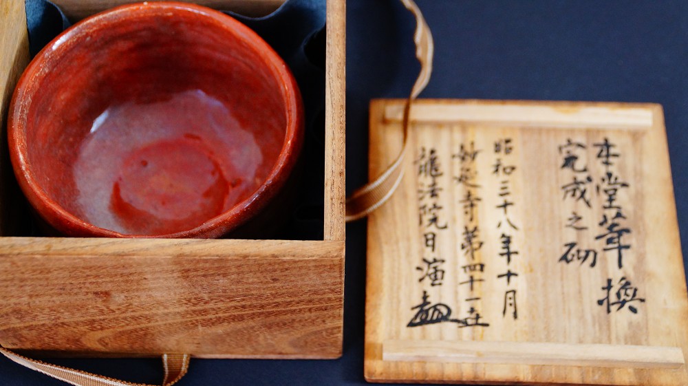 Chawan made of Raku ware by Sairi Hotoku next to the opened lid of the storage box with detailed ink inscription