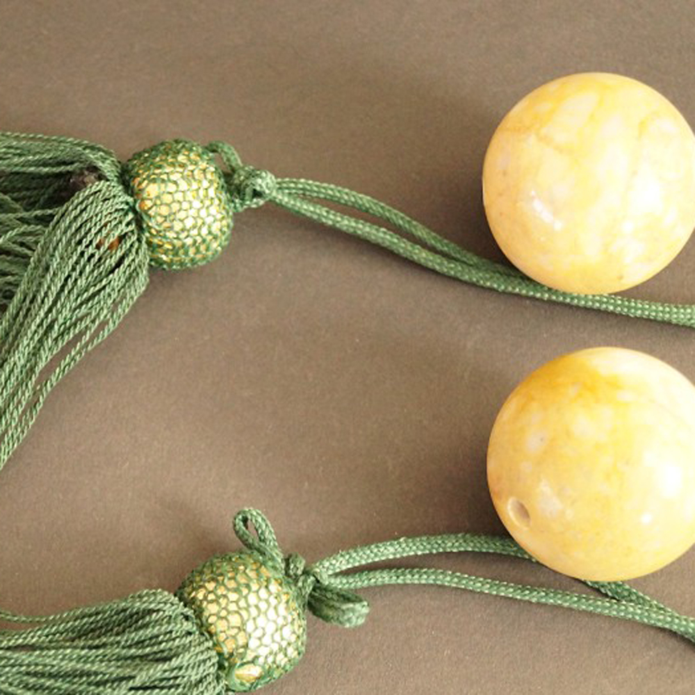 Two yellowish natural stone balls with green silk tassels set close-up preview