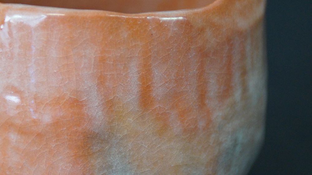 Close-up of the irregularly shaped rim with glossy orange glaze of the Chawan tea bowl made of Raku ware